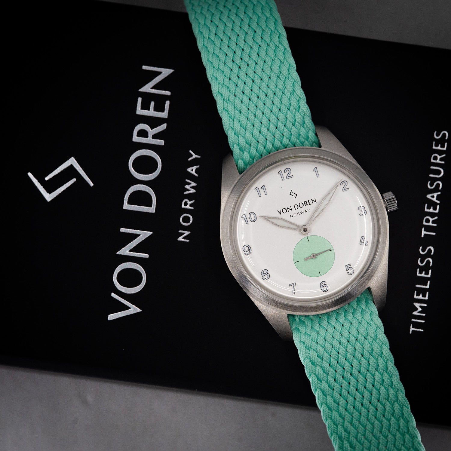 Von Doren Runde Candy Mint-klokke med hvit og mintgrønn tallskive og mintfarget perlonrem, plassert på en sort eske med Von Doren-logo og teksten “Timeless Treasures”.