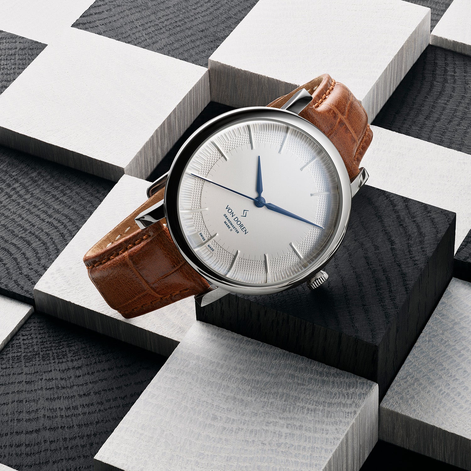Elegant Von Doren-klokke med hvit tallskive og brun rem på grafisk bakgrunn.
