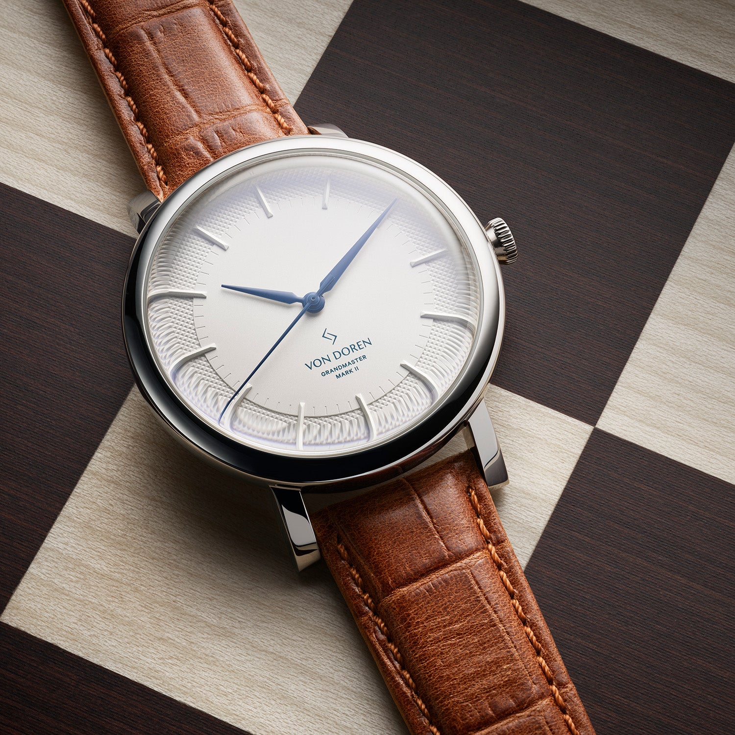Von Doren Grandmaster Mark II med sølvfarget tallskive, blå visere og brun lærrem, plassert på sjakkbrett.