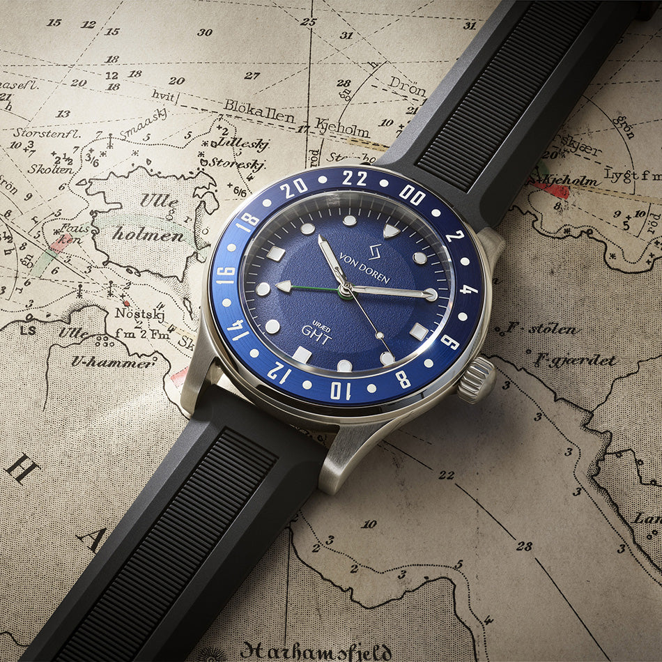 Von Doren klokke med blå skive og sort gummireim, ligger på et kart