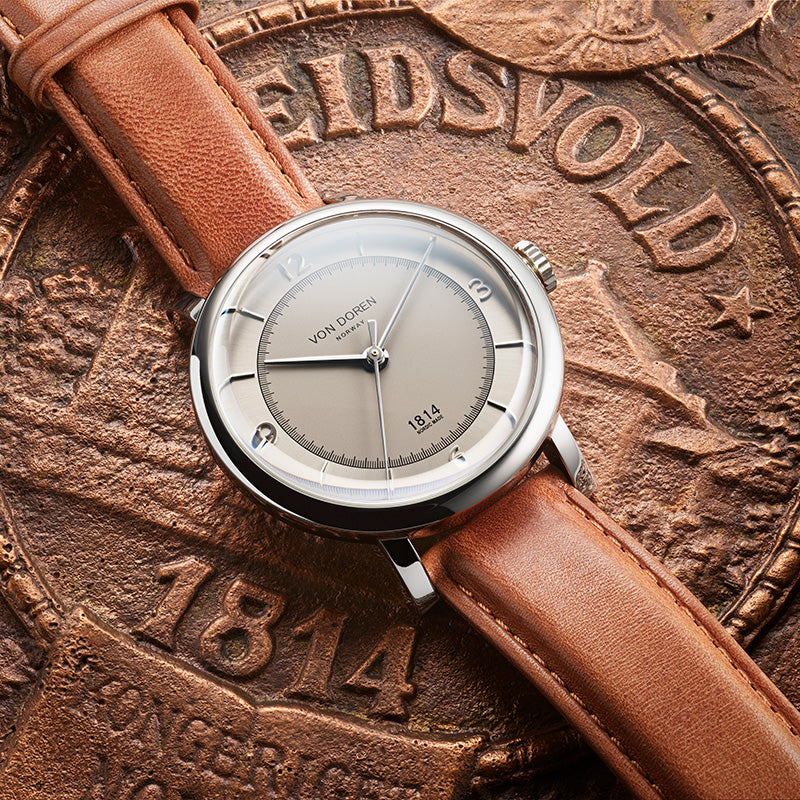 Von Doren 1814 watch with silver dial and brown leather strap resting on a historic medallion with engraved 1814 details. 