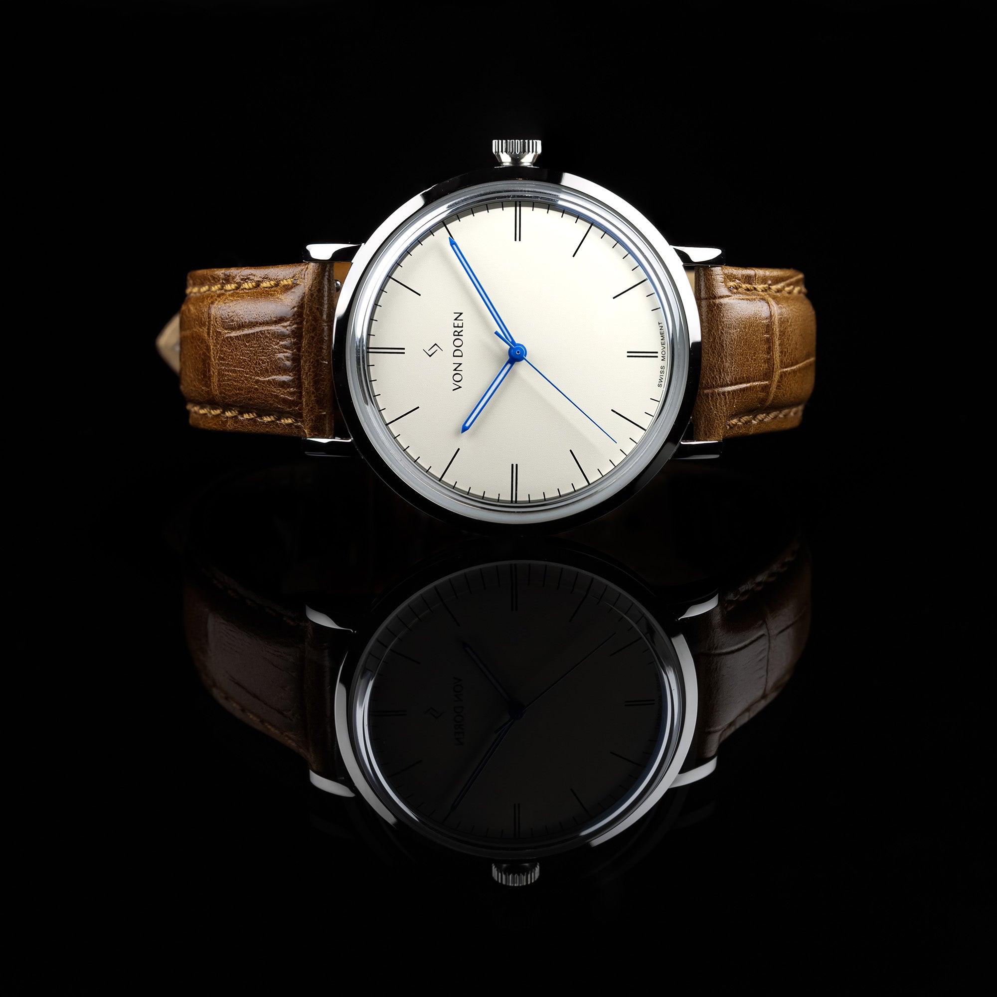 Von Doren klokke liggende på et speil. Modellen heter Aksla og skiven er i fargen antiqu white. Den har brun skinnreim.