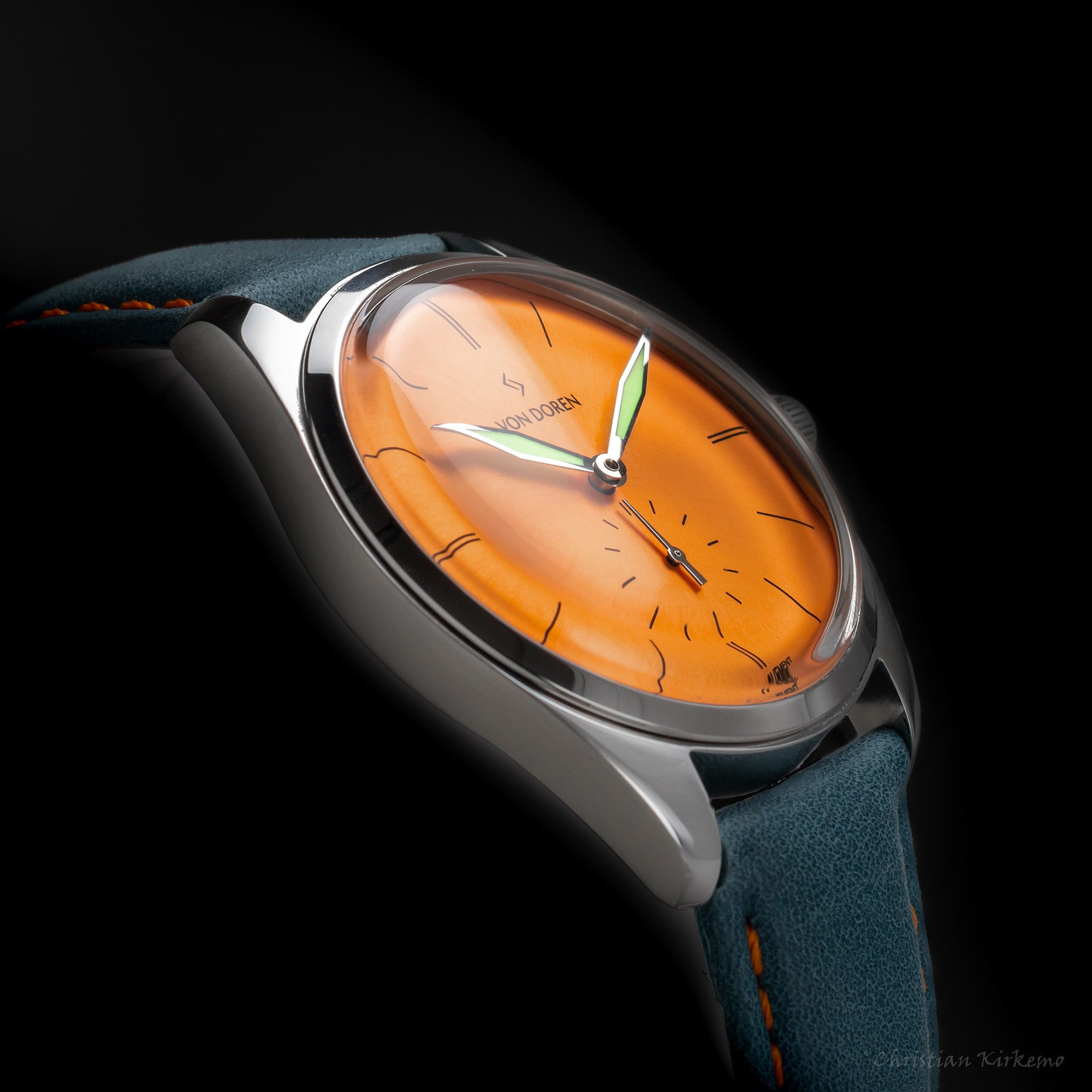 Von Doren-klokke med oransje tallskive og blå skinnrem med oransje søm.