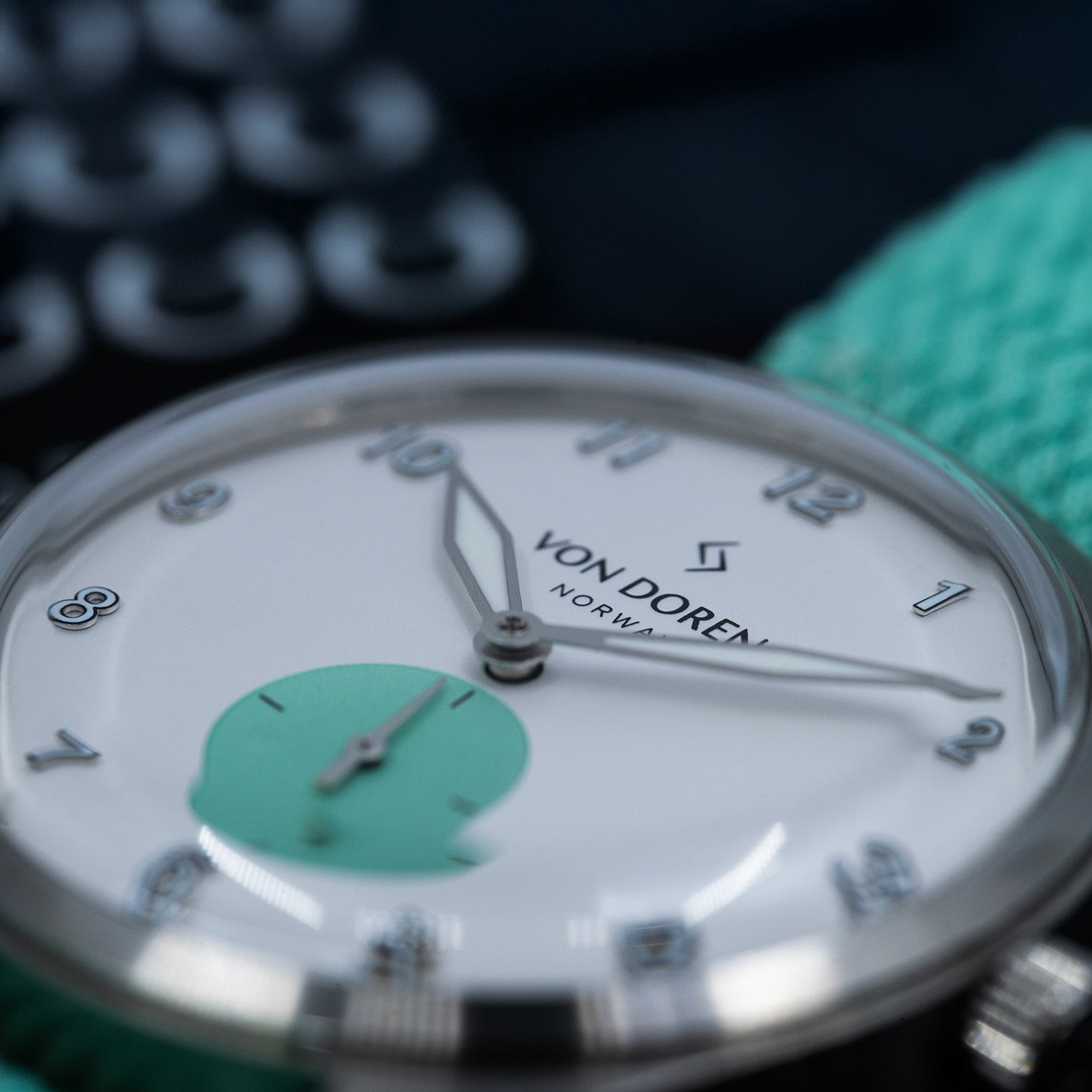  Von Doren Runde Candy Mint-klokke med hvit og mintgrønn tallskive, sølvfargede tall og visere, samt mintfarget perlonrem i bakgrunnen.