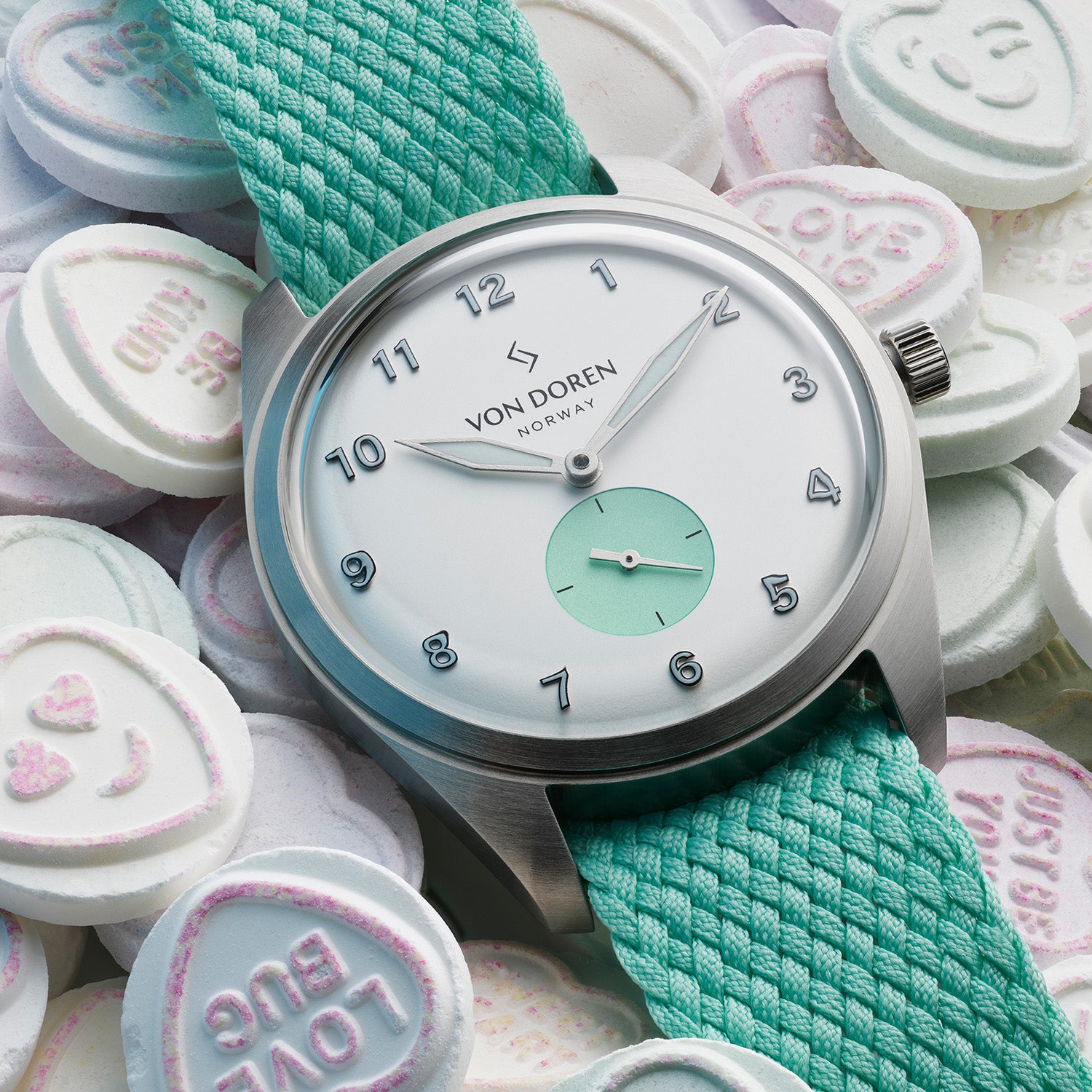 Hvit klokke med grønn perlonstrap liggende oppå loveharts godterier
